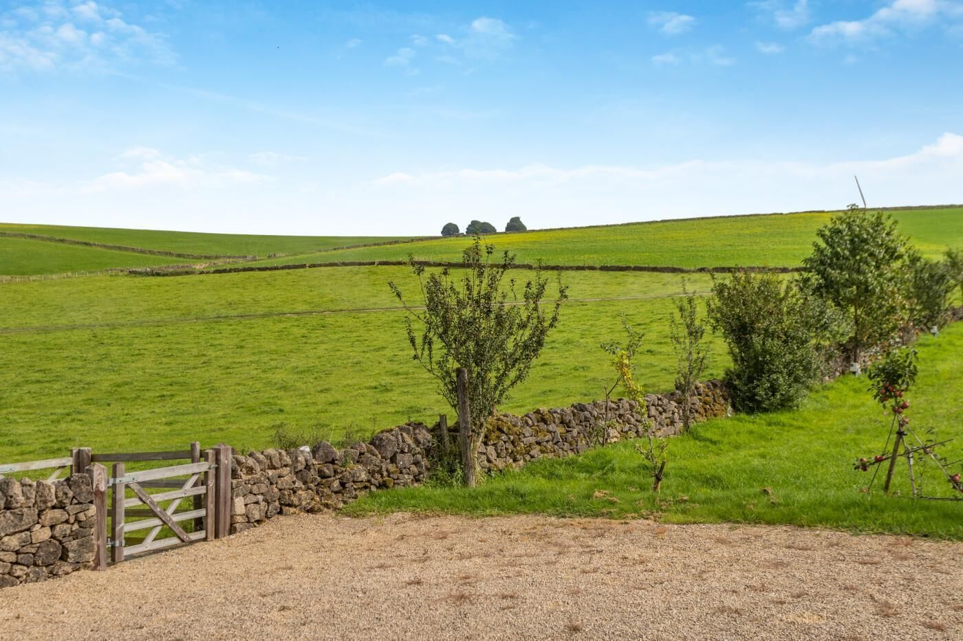 A rural landscape with a stone wall, a wooden gate, and a gravel path.