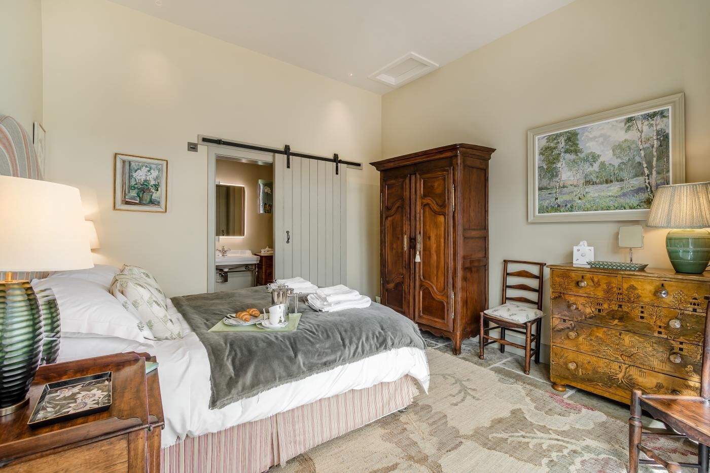A bedroom with a bed, bedside table, dresser, and a painting on the wall.