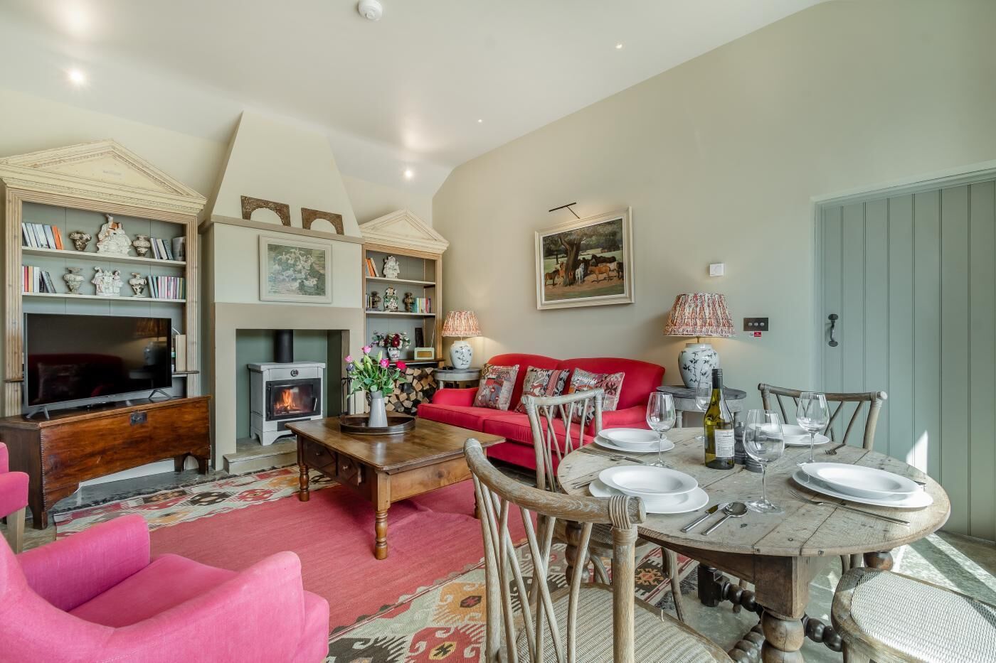 A cozy living room with a fireplace, a red sofa, a dining table set for two, and a television.