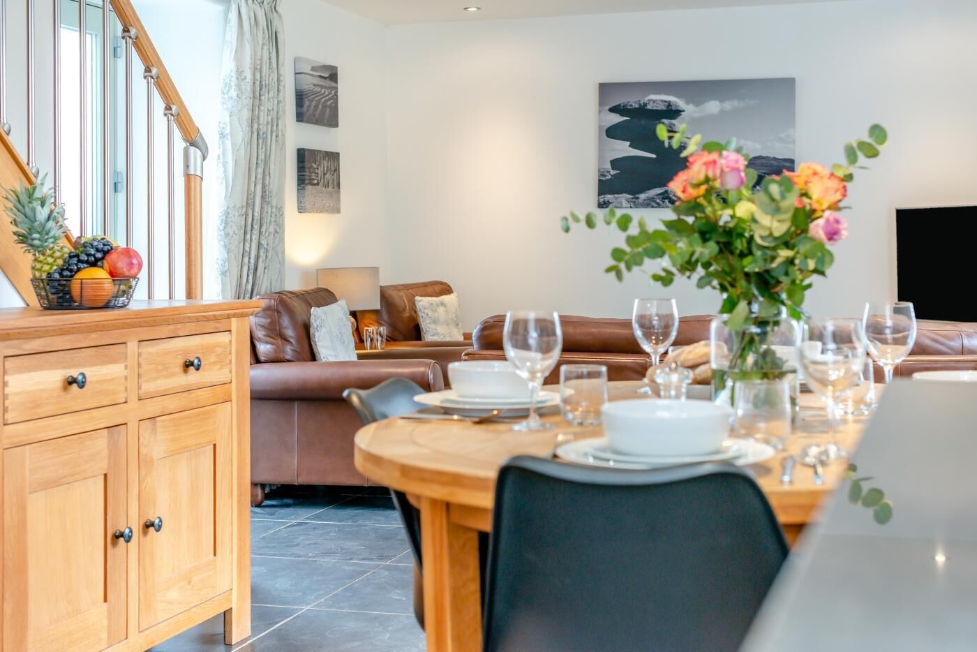 A dining area with a wooden table set for a meal, a brown leather sofa, and a wooden cabinet with drawers.