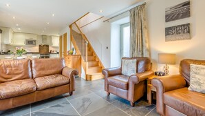 A spacious living room with leather sofas, a wooden staircase, and a kitchen in the background. - 2 Bed in Bodmin (oc-p00378) (Trevisquite Manor)