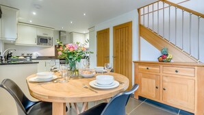 A modern kitchen with a dining table set for four, a microwave, and a fruit basket on the counter. - 2 Bed in Bodmin (oc-p00378) (Trevisquite Manor)