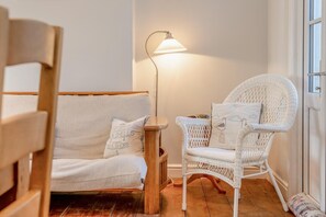 A room with a wicker sofa and chair, a floor lamp, and a view through a window. - 3 Bed in Padstow (oc-p00550) (Padstow)