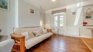 A cozy living room with a wooden floor, a beige sofa with cushions, a white armchair, and a small table. - 3 Bed in Padstow (oc-p00550) (Padstow)
