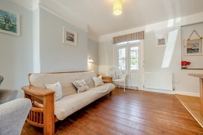 A cozy living room with a wooden floor, a beige sofa with cushions, a white armchair, and a small table. - 3 Bed in Padstow (oc-p00550) (Padstow)