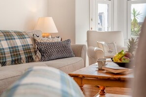 A living room with a sofa, armchair, coffee table, and a lamp. - 3 Bed in Padstow (oc-p00550) (Padstow)