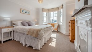 A bedroom with a large bed, bedside tables, a dresser, and a window with a view. - 3 Bed in Padstow (oc-p00550) (Padstow)