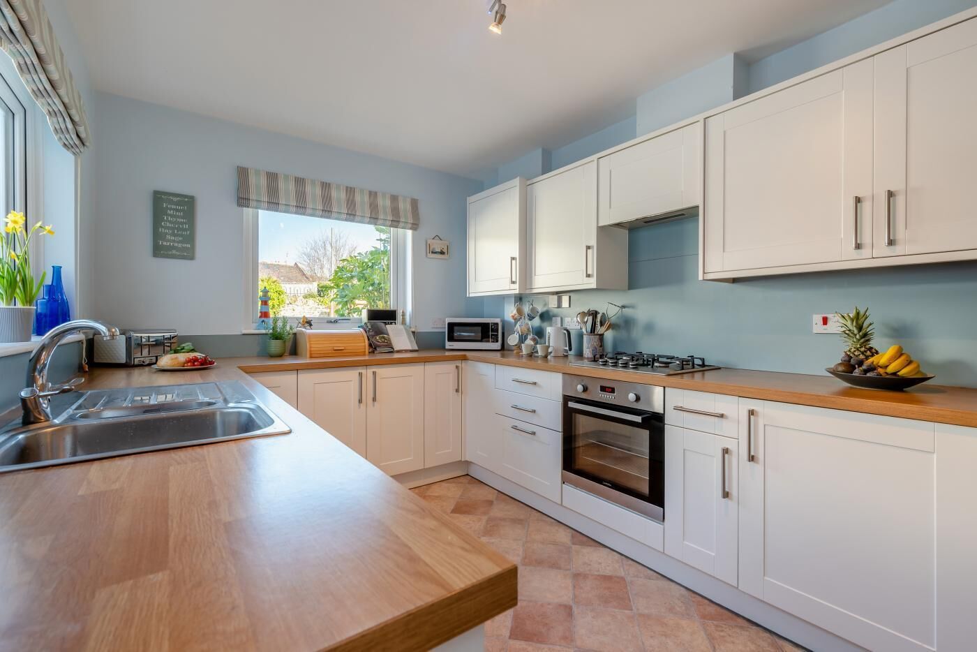 Una cocina moderna con armarios blancos, encimera de madera, horno empotrado y ventana con vistas a zonas verdes.
