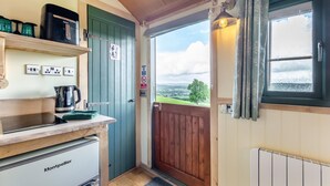 A compact kitchen with a coffee maker, a kettle, and a microwave. A green door leads to a balcony with a view of the countryside. - 1 Bed in Keswick (oc-f33118) (Underskiddaw)