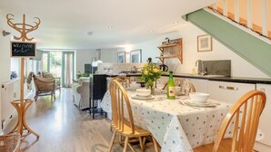 A dining area with a table set for four, surrounded by wicker chairs. A chalkboard sign reads "WELCOME ENJOY".