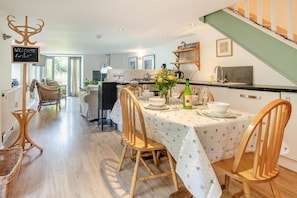 A dining area with a table set for four, surrounded by wicker chairs. A chalkboard sign reads "WELCOME ENJOY".