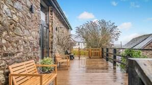 A wooden deck with benches and potted plants, a stone wall, and a view of the surrounding area. - 3 Bed in Dulverton (oc-t32975) (Brushford)