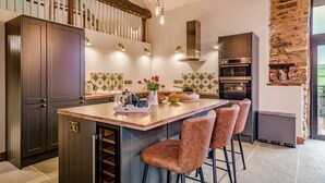 A modern kitchen with a central island, bar stools, and a stone accent wall. - 3 Bed in Dulverton (oc-t32975) (Brushford)