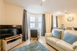 A living room with a television, a sofa, a chair, and a dining area with a table set for two. - 2 Bed in Scarborough (oc-s509) (Scarborough)