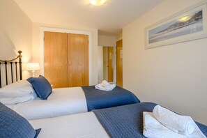 A hotel room with two beds, a wooden wardrobe, a framed picture on the wall, and a lamp on the nightstand. - 2 Bed in Scarborough (oc-s509) (Scarborough)