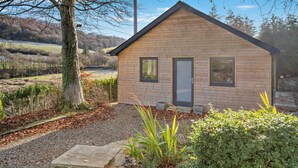 A small wooden cabin with a door and windows, surrounded by gravel and plants. - 3 Bed in Defynnog (oc-p33133) (Defynnog)