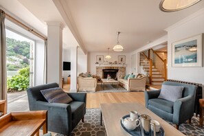A spacious living room with a fireplace, two sofas, a coffee table, and a view of greenery outside.
