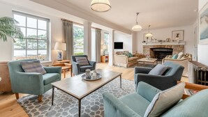 Un salon spacieux doté d’une cheminée, de sièges confortables et de grandes fenêtres offrant une vue sur l’extérieur.