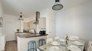 Una cocina moderna con armarios blancos, una isla central con taburetes y un comedor con mesa de vidrio para seis.