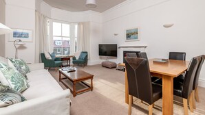 Ein Wohnzimmer mit Sofa, Sesseln, Couchtisch, Fernseher und Kamin.