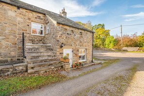 A stone house with a front door, a small porch, and a gravel driveway. - 2 Bed in West Blackdene (oc-r33034) (Ireshopeburn)