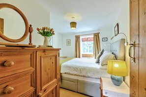 A bedroom with a wooden dresser, a bed with a headboard, a bedside table with a lamp, and a window with curtains. - 2 Bed in West Blackdene (oc-r33034) (Ireshopeburn)