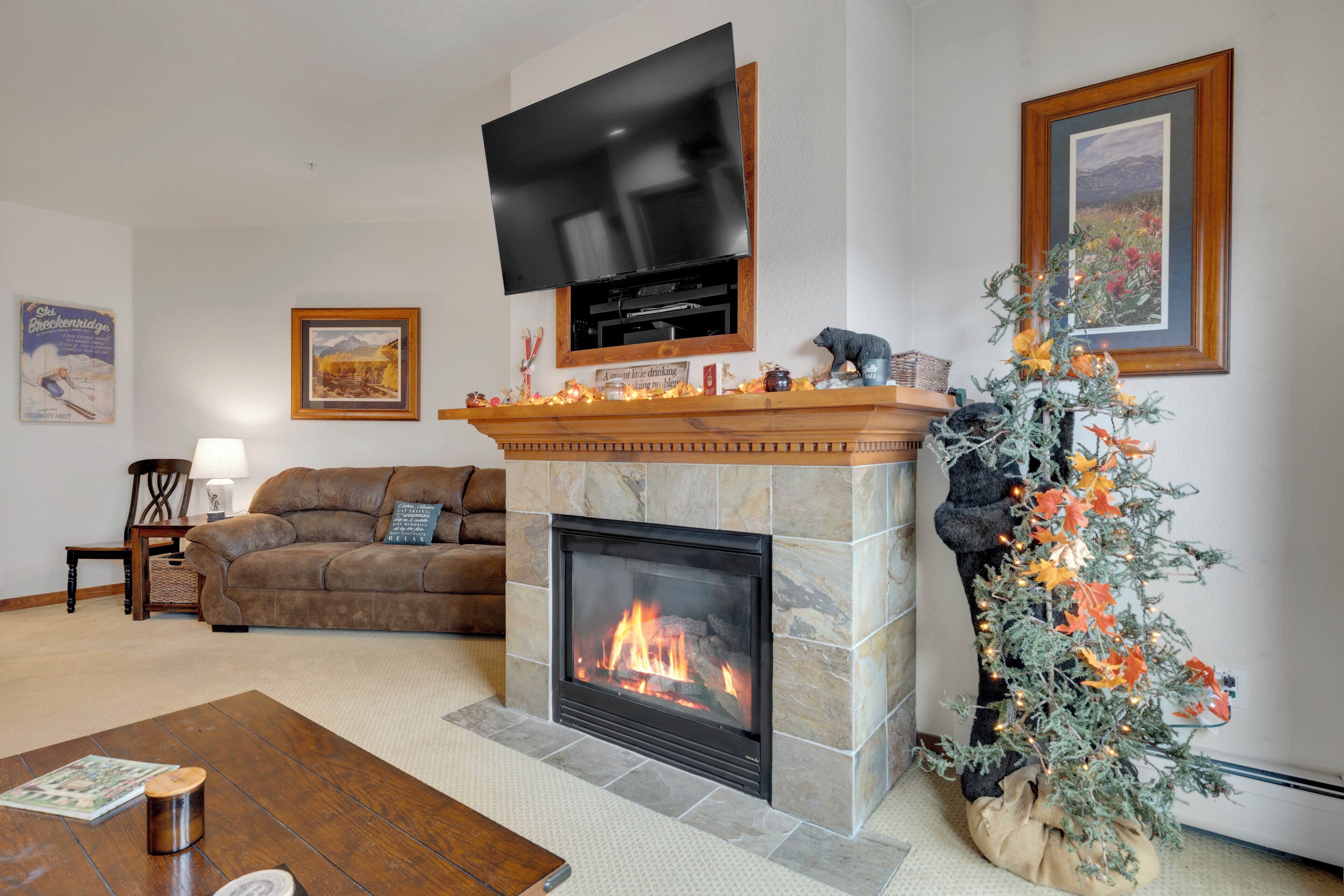 Una sala de estar con chimenea de piedra, un televisor montado encima y un árbol de Navidad, además de un sofá.