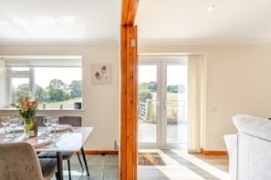 A dining area with a table set for four, a sofa, and a view of the outdoors through large windows.