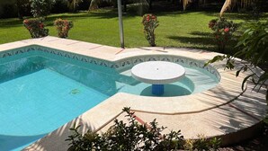 Zwembad met een jacuzzi, omringd door een tuin met palmstruiken en bloeiende planten.