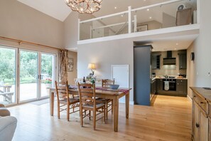 A spacious dining area with a wooden table and chairs, a kitchen with dark cabinets, and a view of the outdoors through large sliding glass doors. - 1 Bed in Twyford (oc-c33411) (Twyford)