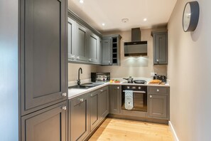 A compact kitchen with grey cabinets, a microwave, a stove, and a clock on the wall. - 1 Bed in Twyford (oc-c33411) (Twyford)