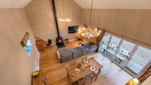 Un loft espacioso con techo alto, chimenea, un sofá grande, una mesa de comedor y vistas amplias por grandes ventanales.