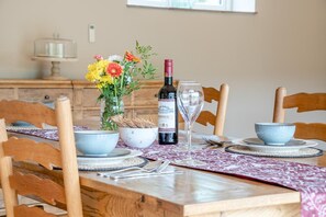 A dining table set with a wine bottle, a glass, bowls, and a vase with flowers. - 1 Bed in Twyford (oc-c33411) (Twyford)