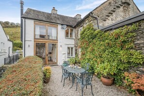A two-story house with a stone exterior, a wooden door, and a gravel patio with a table and chairs. - 2 Bed in Troutbeck (oc-c33392) (Troutbeck)