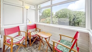 A sunlit room with large windows, a wooden table, and two red chairs with patterned cushions. - 3 Bed in Paignton (oc-bc1890) (Paignton)