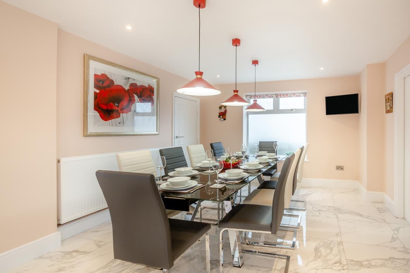 A dining area with a long table set for six, white chairs, and red pendant lights.