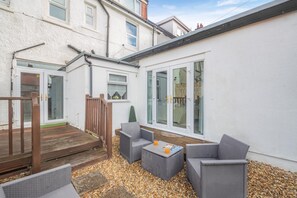 A residential property with a patio area featuring outdoor furniture, a wooden deck, and a white exterior wall. - 6 Bed in Llandudno (oc-s33417) (Llandudno)