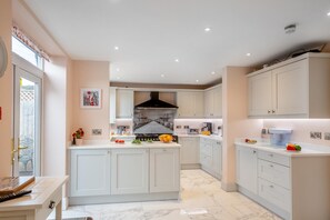 A modern kitchen with white cabinetry, a central island, and a view into the dining area. - 6 Bed in Llandudno (oc-s33417) (Llandudno)