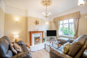 A living room with leather sofas, a fireplace, a flat-screen TV, and a glass coffee table. - 6 Bed in Llandudno (oc-s33417) (Llandudno)