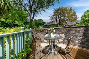 An outdoor patio with a stone wall, a wooden deck, and a table set for dining. - 2 Bed in Bere Alston (oc-bctang) (Bere Alston)