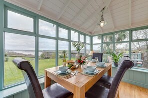 Ein Wintergarten mit Esstisch für vier Personen, großen Fenstern und Blick ins Freie.