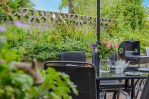 Un área de comedor al aire libre con una mesa lista para dos personas, rodeada de abundante follaje y un muro de piedra.