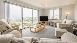 Een ruime woonkamer met een grote televisie, comfortabele zithoek en uitzicht op een stadsbeeld.