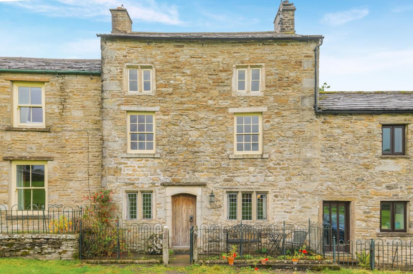 A stone building with multiple windows, a wooden door, and a metal fence with potted plants.