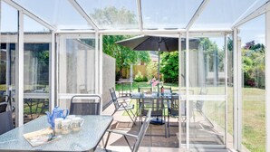 A conservatory with a glass table and chairs, a patio umbrella, and a view of a garden. - 2 Bed in Paignton (oc-h28353) (Paignton)