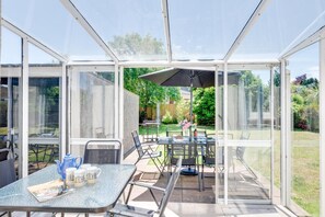 A conservatory with a glass table and chairs, a patio umbrella, and a view of a garden. - 2 Bed in Paignton (oc-h28353) (Paignton)