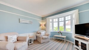A living room with a sofa, armchair, TV stand, and a window with curtains. - 2 Bed in Paignton (oc-h28353) (Paignton)
