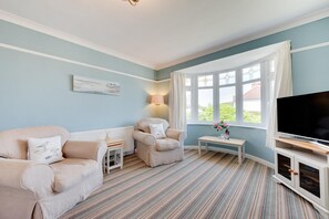 A living room with a sofa, armchair, TV stand, and a window with curtains. - 2 Bed in Paignton (oc-h28353) (Paignton)