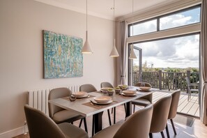 A dining area with a large table set for six, a modern pendant light, and a view of a vineyard through large windows. - 4 Bed in Coleford (oc-t33302) (Coleford)