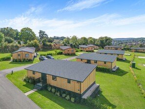 A row of modern, single-story cabins with flat roofs, arranged in a neat row on a well-maintained lawn. - 4 Bed in Coleford (oc-t33302) (Coleford)